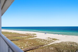 Blick auf einen Strand mit einem hölzernen Promenadenweg, blauem Himmel und ruhiger See.