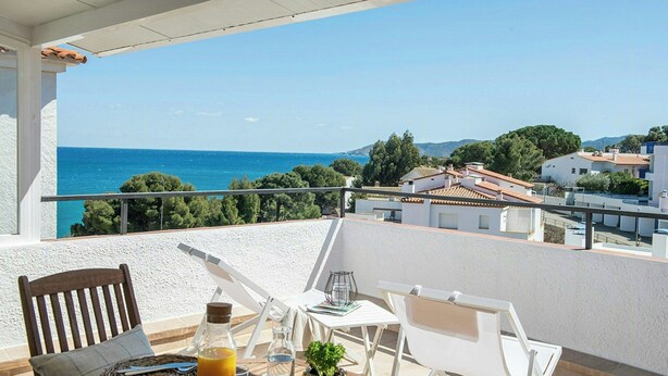 Un balcón con mesa, sillas y vista al mar y edificios.