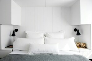A neatly made bed with white bedding and pillows, two black bedside lamps, and a woven basket on the nightstand. - Designed Costa Brava flat with panoramic sea views (Girona)