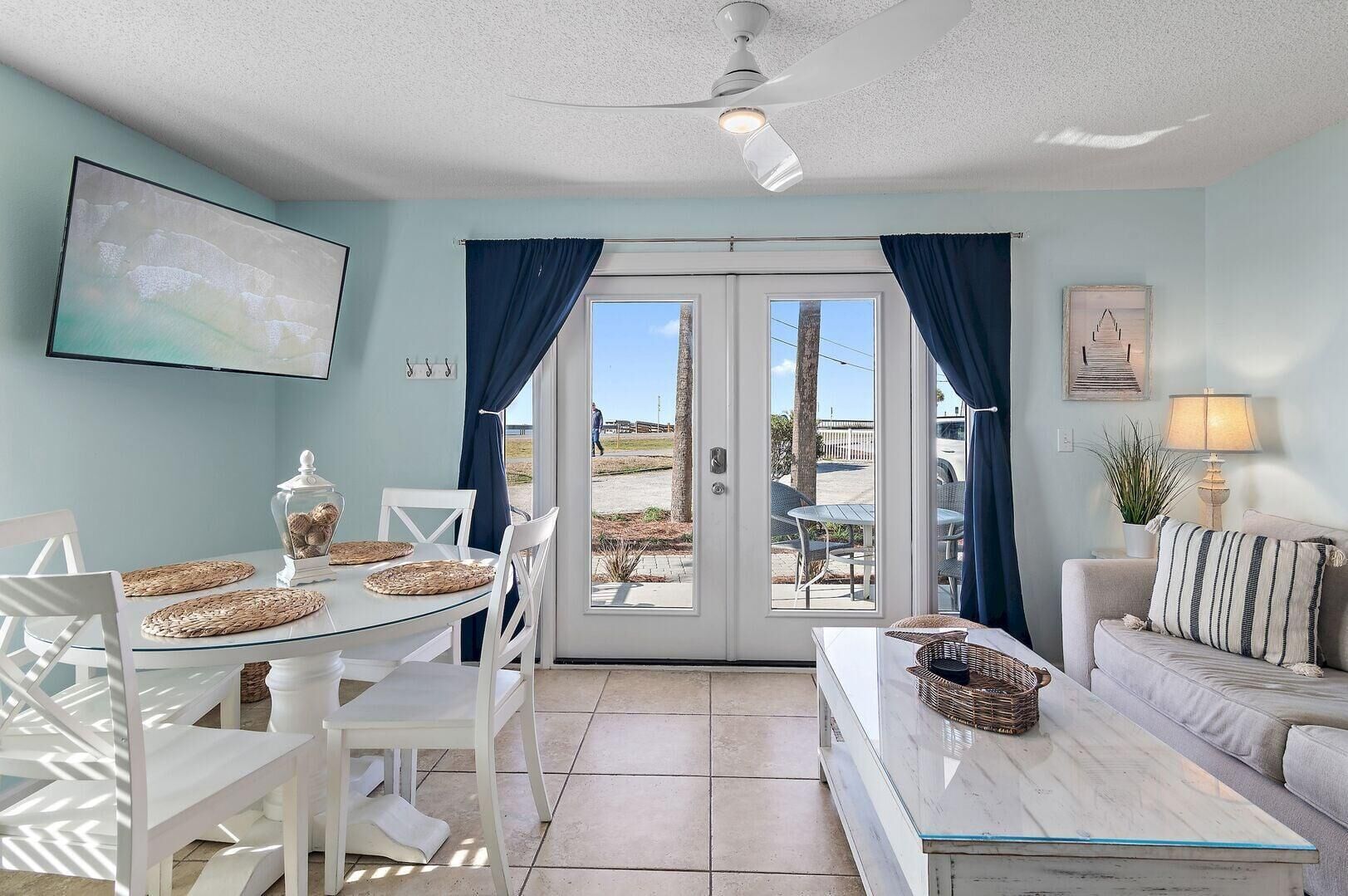A room with a dining table, chairs, a sofa, a lamp, and a view through a glass door.