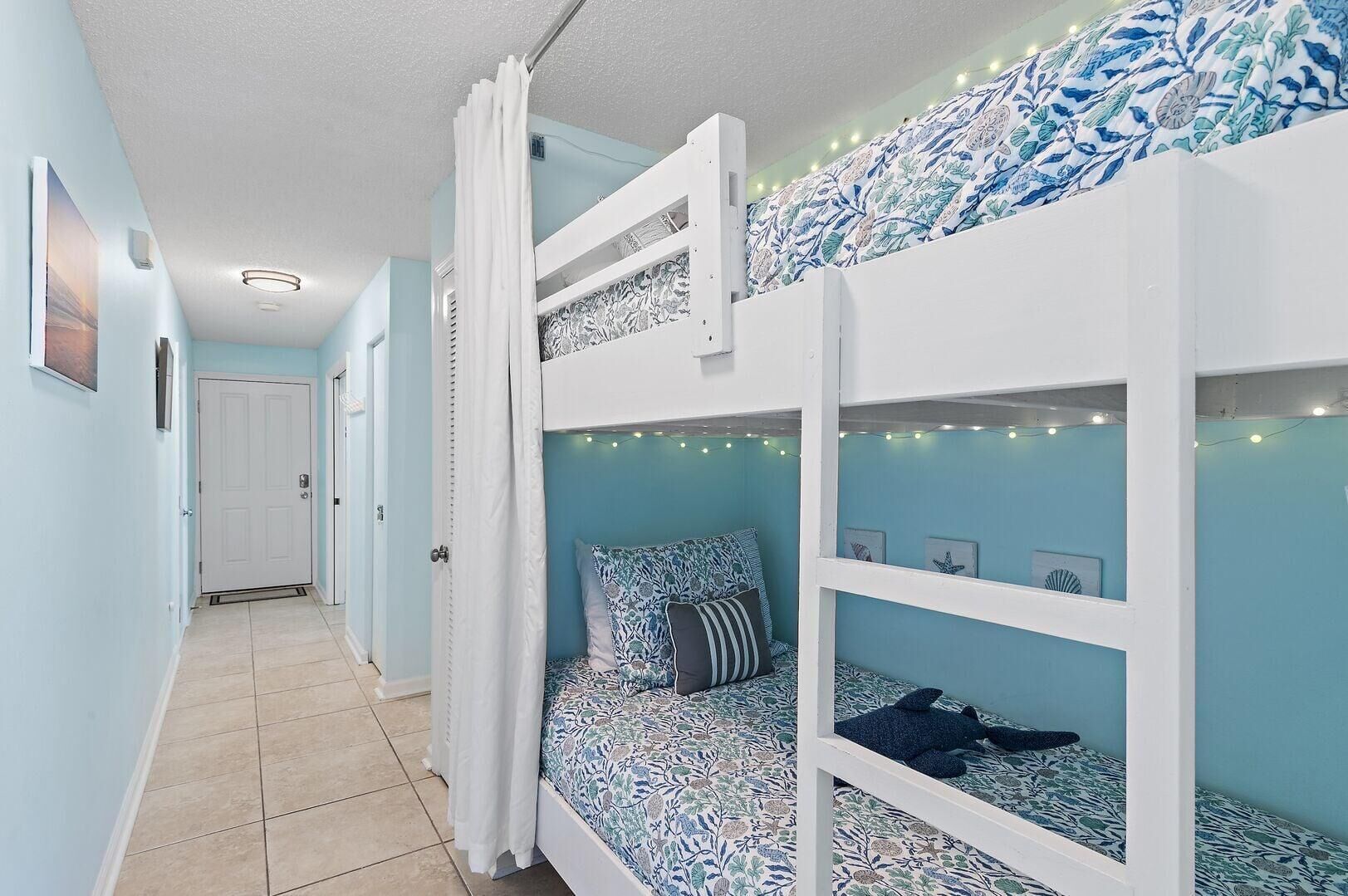 A bunk bed room with a patterned bedspread, a curtain, and string lights.