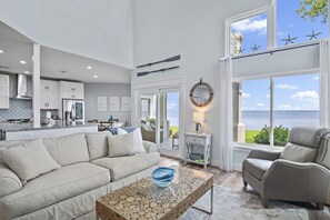 Ein geräumiger Wohnbereich mit einer großen Couch, einem Couchtisch und Meerblick durch große Fenster.