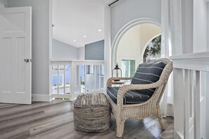 Ein Korbstuhl mit Kissen, ein gewebter Hocker und Blick aufs Meer vom Balkon aus.