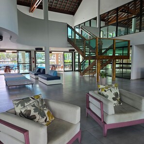 Eine geräumige Lobby mit moderner Treppe, Sitzbereichen und großen Fenstern mit Blick auf den Außenpool.