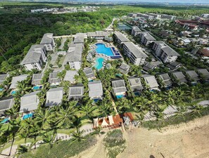 Eine Vogelperspektive zeigt ein Resort mit mehreren Gebäuden, einem zentralen Swimmingpool und umliegenden Palmen.