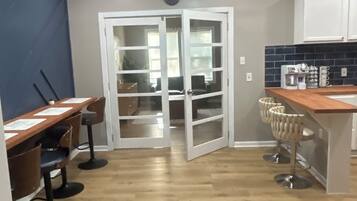 A kitchen with a wooden countertop, bar stools, a ceiling fan, and a door leading to another room.