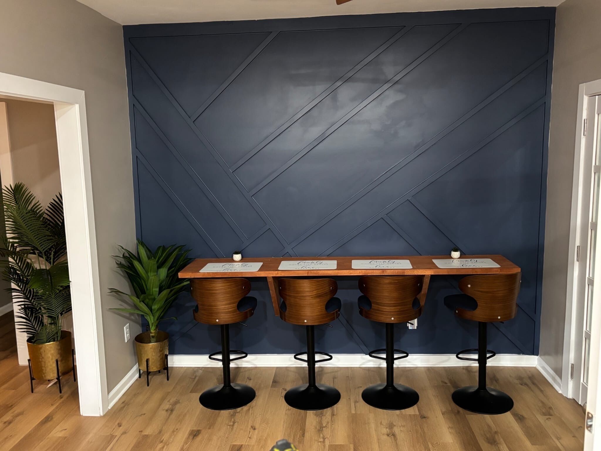 Un espace bar avec un mur bleu foncé, un comptoir en bois et quatre tabourets.