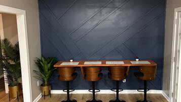 Un espace bar avec un mur bleu foncé, un comptoir en bois et quatre tabourets.