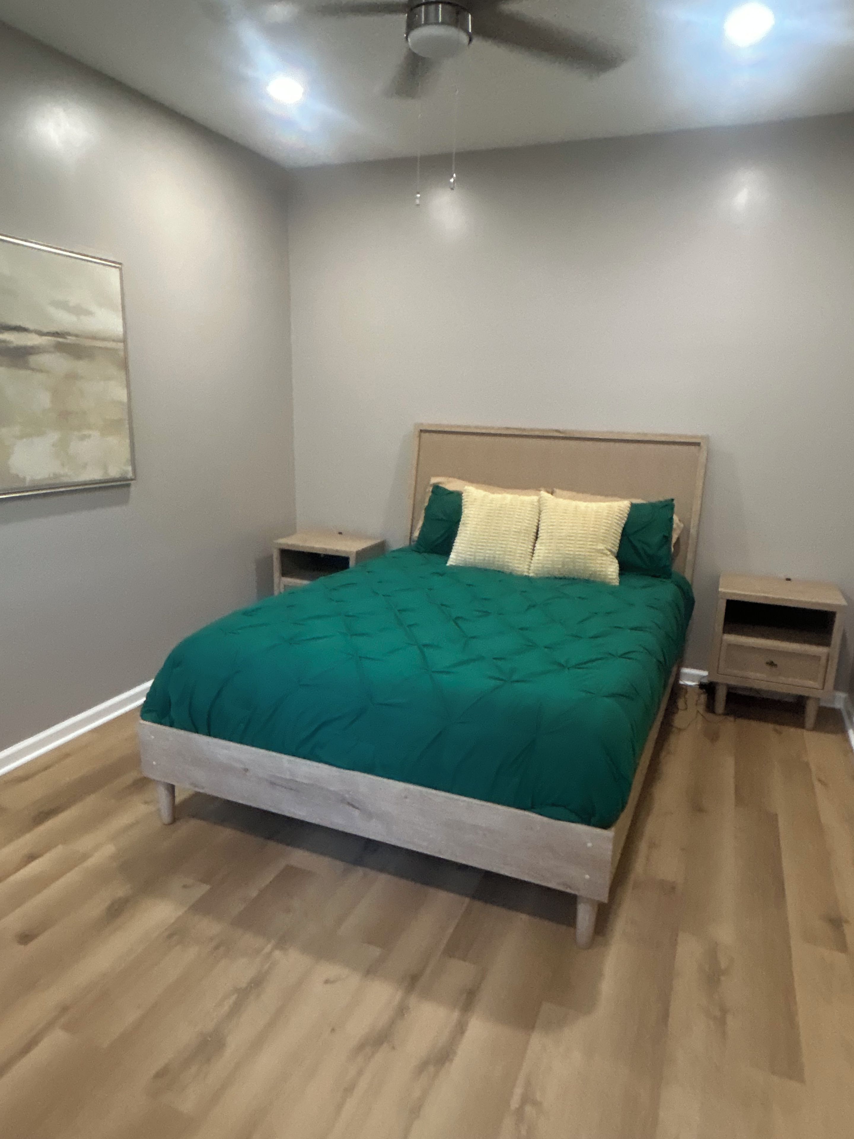 A bedroom with a bed, nightstands, a ceiling fan, and a wall-mounted artwork.