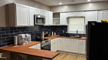 Une cuisine moderne avec des meubles blancs, un pare-feu noir en carreaux, un plan de travail en bois et un réfrigérateur noir.