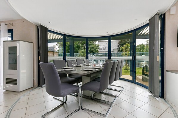 Un'area pranzo moderna con soffitto curvo, un tavolo grande apparecchiato per sei persone e vista su un giardino attraverso delle porte in vetro.