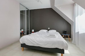 Un dormitorio moderno con una cama, una mesita de noche, una silla y un ventanal grande.
