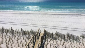 Ein Strand mit einer Holzpromenade, die zum Meer führt, Sanddünen und einem strahlend blauen Himmel.