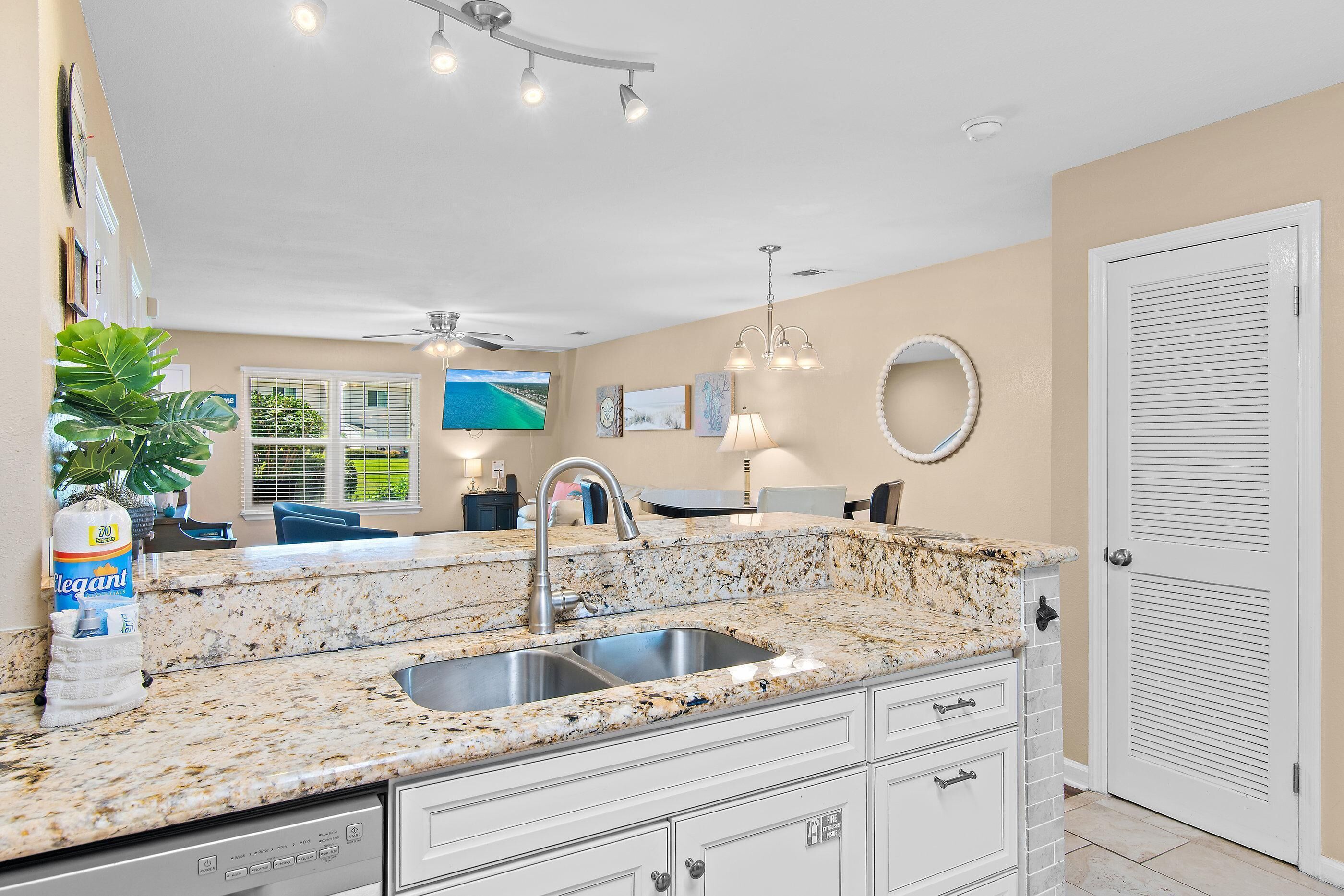 A kitchen with granite countertops, a stainless steel sink, a ceiling fan, and a dining area with a TV.
