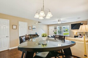 Ein moderner Essbereich mit einem Glastisch, Ledersesseln, einer Chandelierleuchtreife und Blick ins Freie.