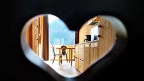A heart-shaped window framing a kitchen with wooden cabinets, a dining table, and a view of a mountain.