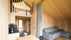 A compact, wooden interior with a loft bedroom, a sofa, a dining table, and a kitchen area.