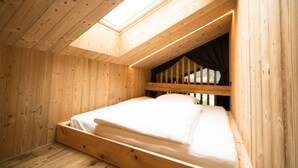 A wooden room with a sloped ceiling, a bed, and a skylight.