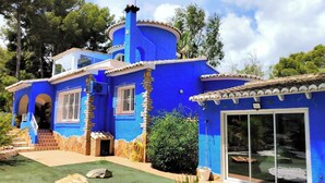 Ein blaues Haus mit einem runden Turm, einer Terrasse mit Steinen und einem Garten.