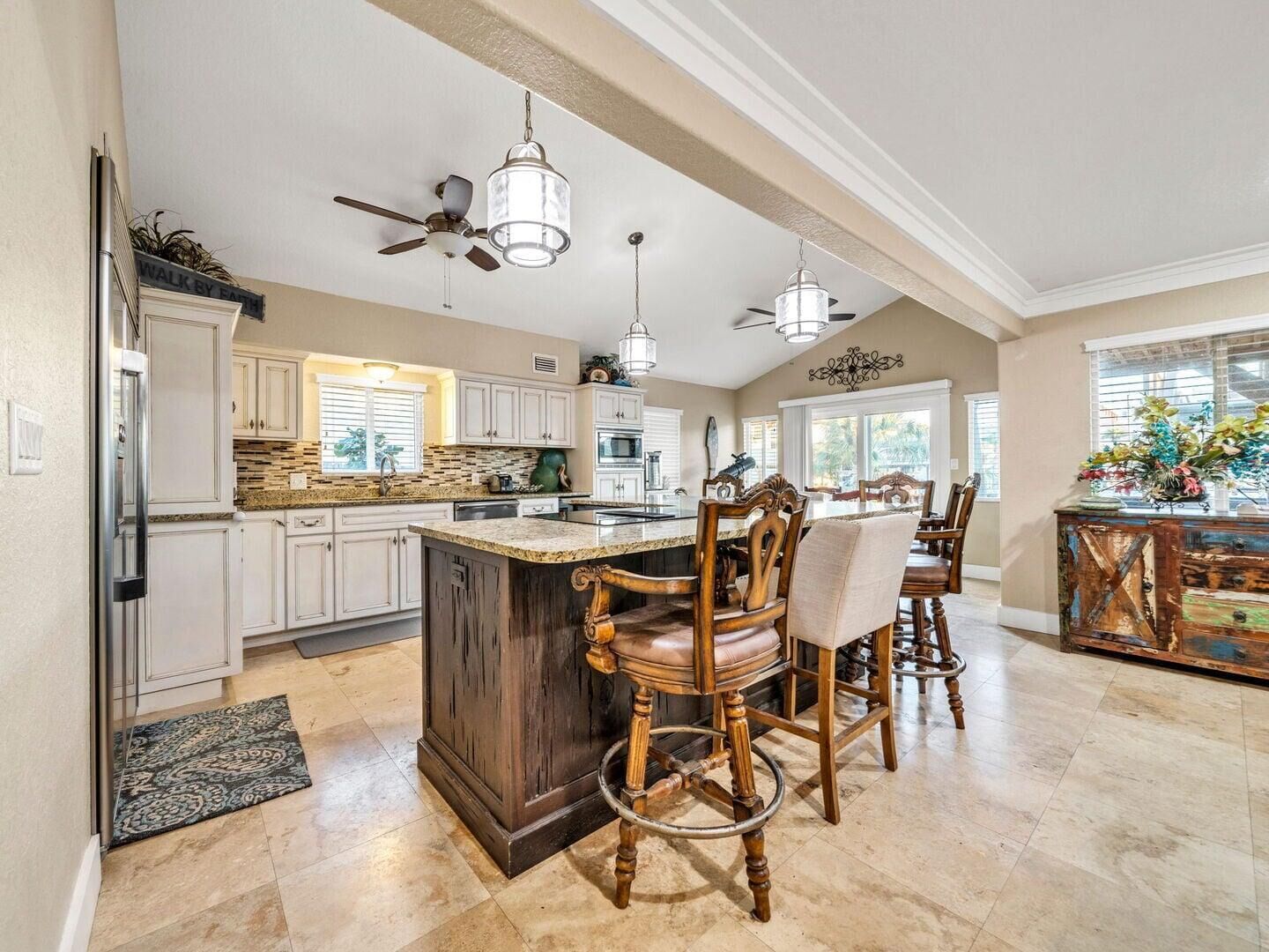 A spacious kitchen with a large island, white cabinetry, and a dining area with wooden chairs.