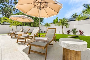 A patio area with wooden lounge chairs, beige umbrellas, and a stone table. - A Touch of Heaven • Heated Pool • Near Beach (Naples)