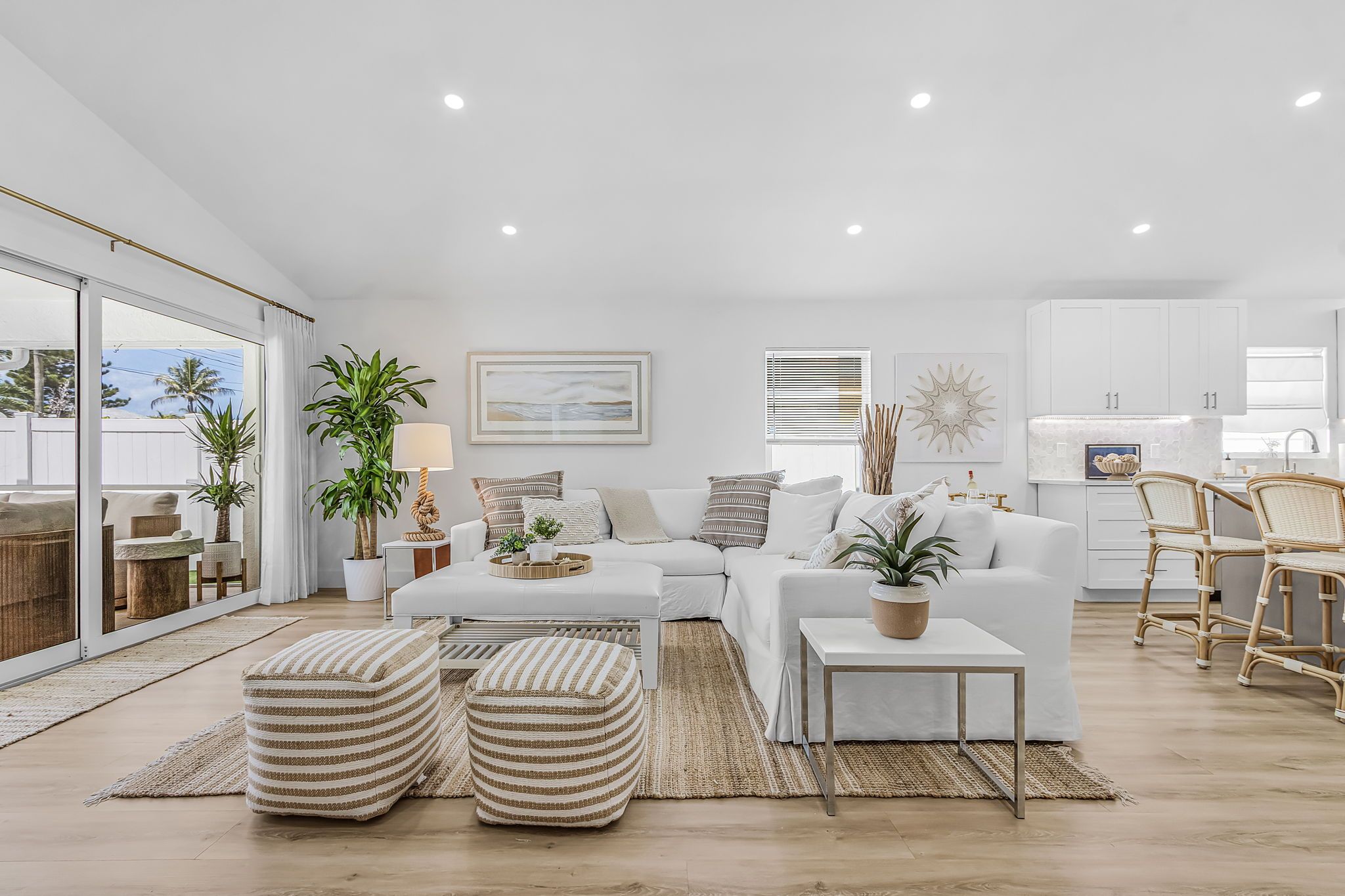 A modern living room with a white sofa, ottomans, and a dining area with wicker chairs.