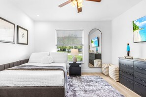 A modern bedroom with a bed, bedside table, lamp, mirror, dresser, and artwork on the walls. - A Touch of Heaven • Heated Pool • Near Beach (Naples)