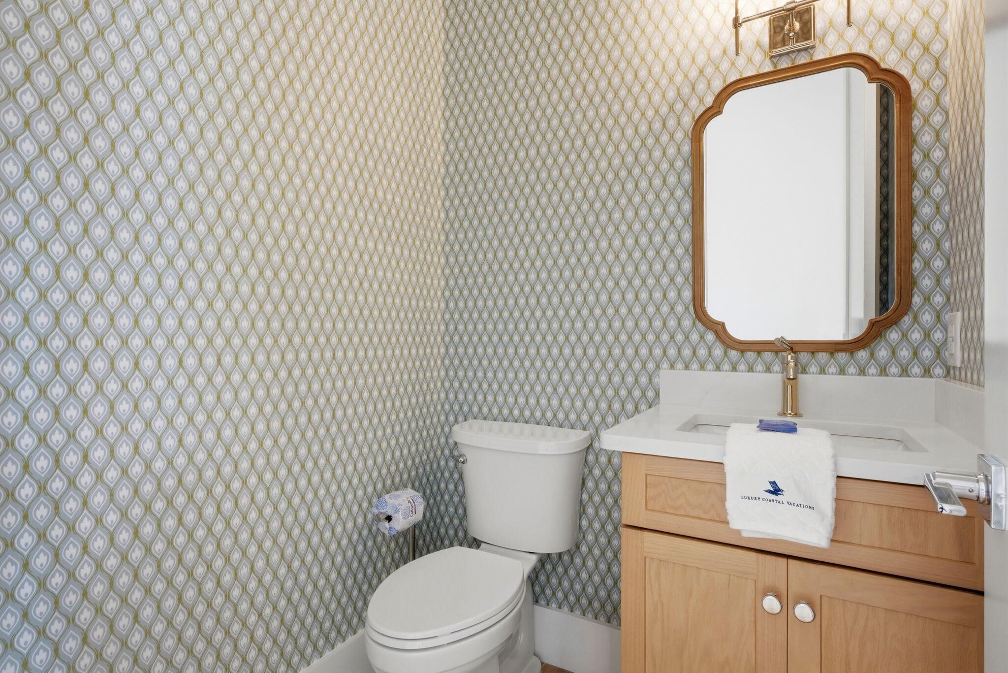 Baño con inodoro, lavamanos, espejo y papel tapiz estampado.