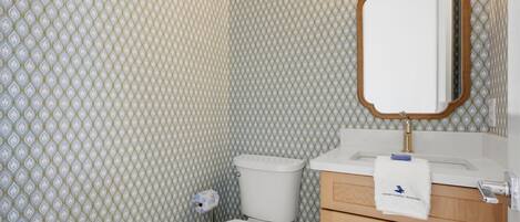 Baño con inodoro, lavamanos, espejo y papel tapiz estampado.