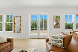 Ein geräumiges Wohnzimmer mit einem braunen Ledersofa, einem Couchtisch und einem großen Fenster mit Blick auf Grünflächen.