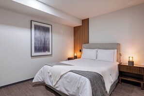 Ein modernes Hotelzimmer mit einem großen Bett, einer Wandpaneele aus Holz, gerahmten Kunstwerken und Nachttischlampen.