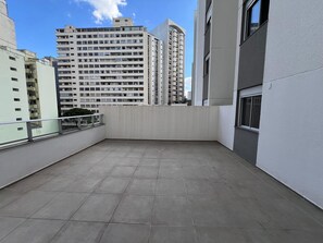 A rooftop terrace with a tiled floor, a railing, and a view of surrounding high-rise buildings.