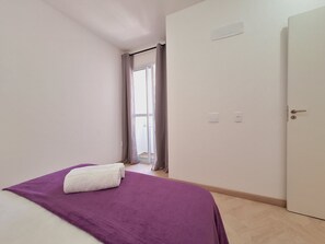 A room with a bed, a door, a window with curtains, and a light switch on the wall. - LK Centro 6 (Belo Horizonte)