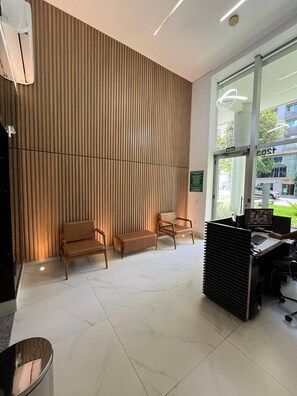 A reception area with a wooden slatted wall, two wooden chairs, a bench, a reception desk with a computer, and a large window with a view of the street.