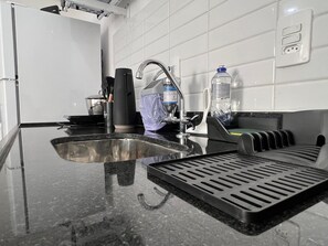 Eine Küche mit Spüle aus Edelstahl, einem Wasserhahn, einer Wasserflasche und einem Mülleimer.