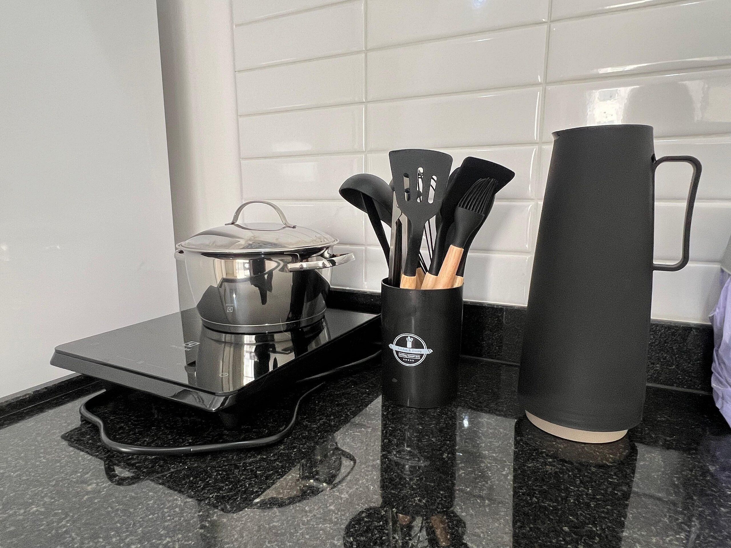 Una encimera de cocina con estufa, una olla con tapa, cafetera, taza y un recipiente para utensilios.