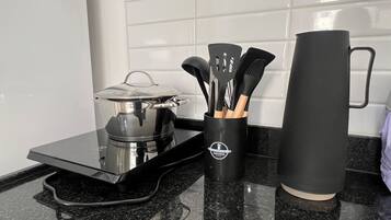 Una encimera de cocina con estufa, una olla con tapa, cafetera, taza y un recipiente para utensilios.