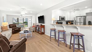 Een moderne woonkamer met een flatscreen televisie, leren fauteuils, een salontafel en een eethoek met barstoelen.