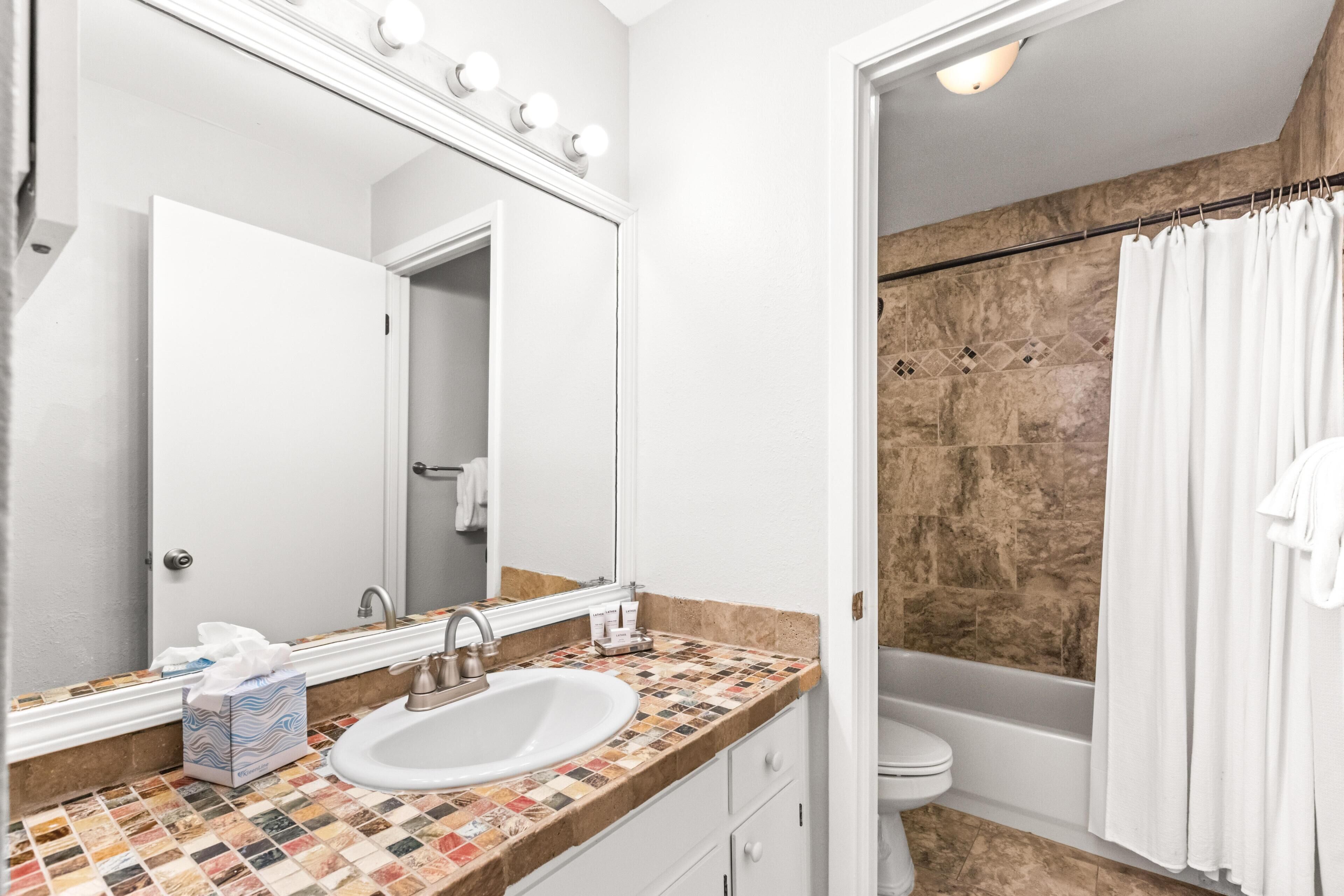 A bathroom with a white sink, a mirror with lights, a tiled shower area, and a bathtub.
