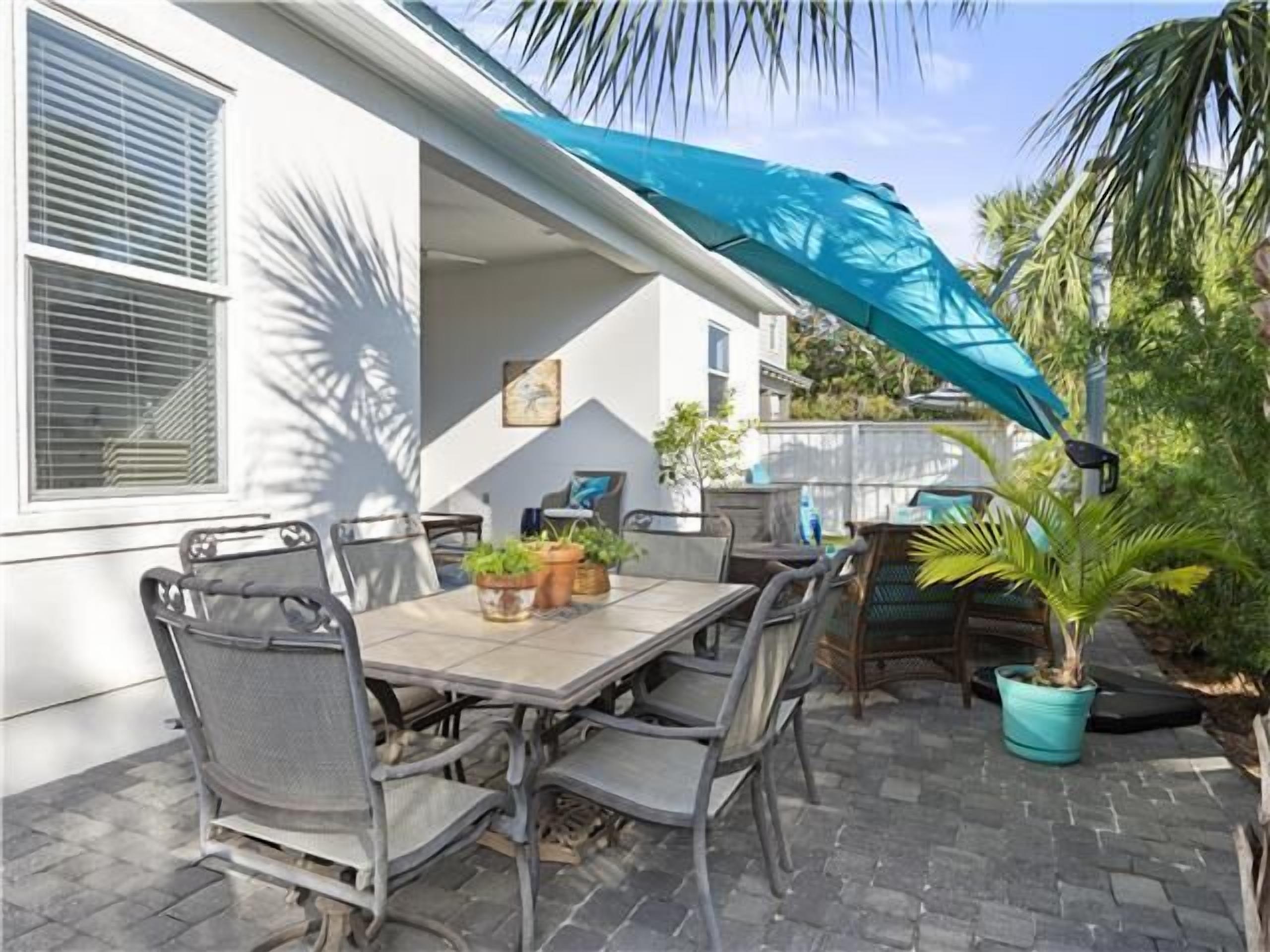 An outdoor patio with a table and chairs, a blue canopy, and potted plants.