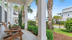 A covered outdoor area with wooden chairs, palm trees, and a view of residential buildings. - Frangista Beach: Whispering Palms (Miramar Beach)