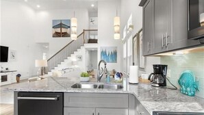 A modern kitchen with a central island, stainless steel appliances, and a staircase leading to an upper level. - Frangista Beach: Whispering Palms (Miramar Beach)