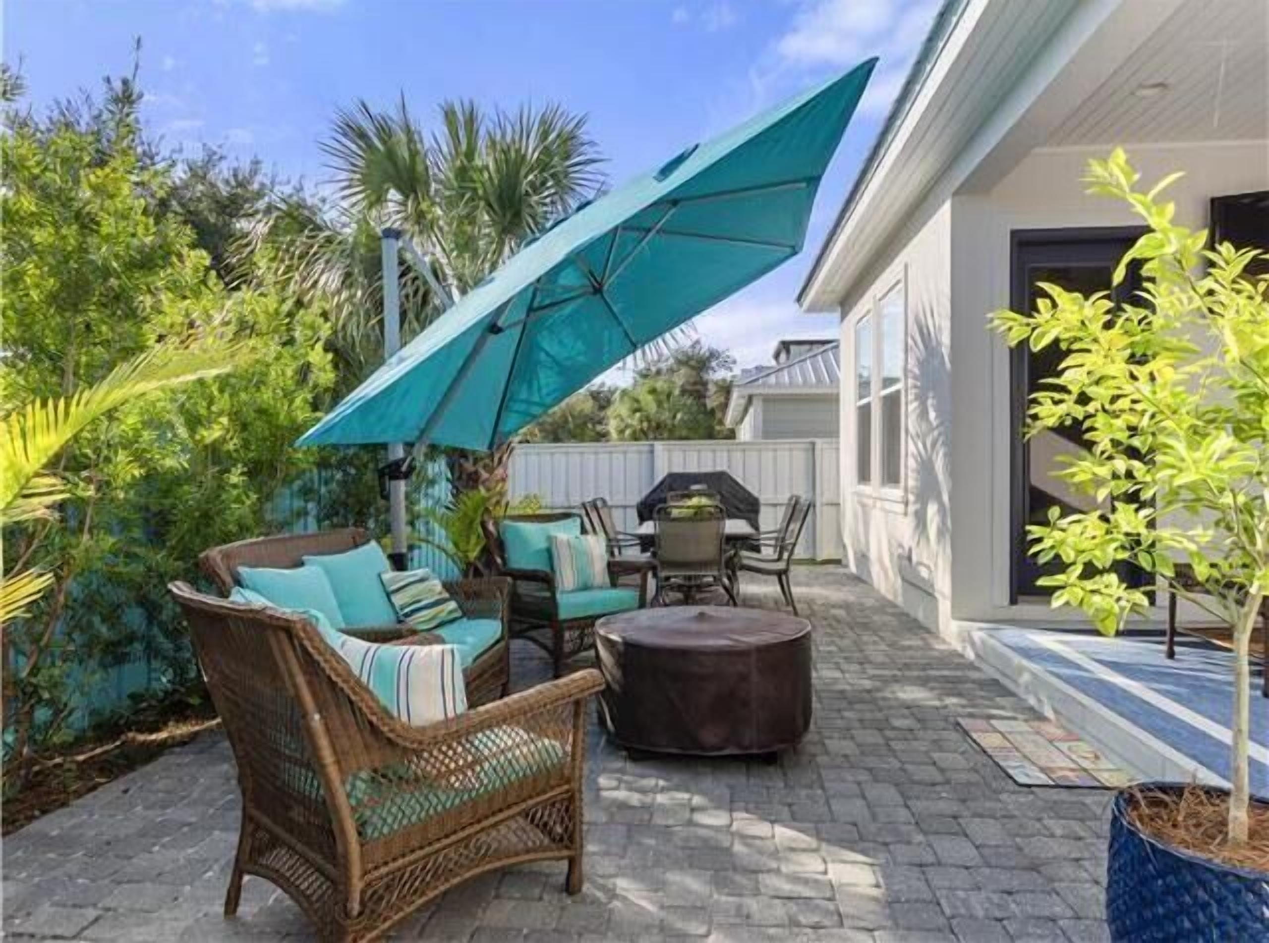 Une terrasse dotée de meubles en osier, d’une table et d’un grand parasol.