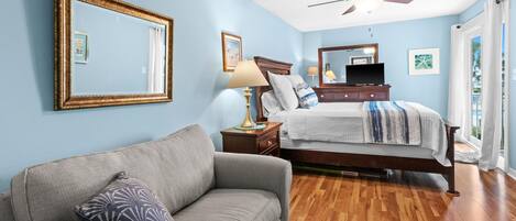 A bedroom with a bed, a nightstand, a lamp, a ceiling fan, and a large mirror.
