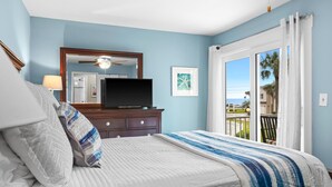 A bedroom with a bed, a dresser, a television, and a balcony with a view. - Tradewinds Condominium #25 (Miramar Beach)