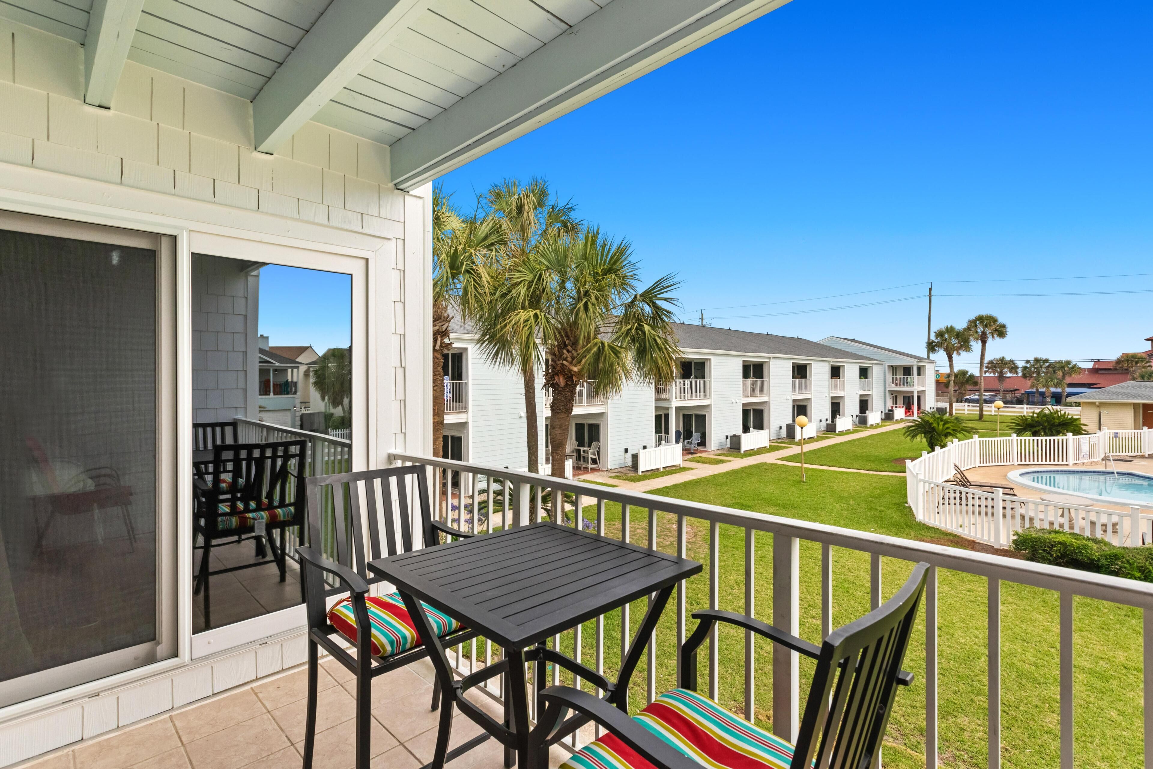 A balcony with a table and chairs, a pool, and a view of a building with multiple windows.