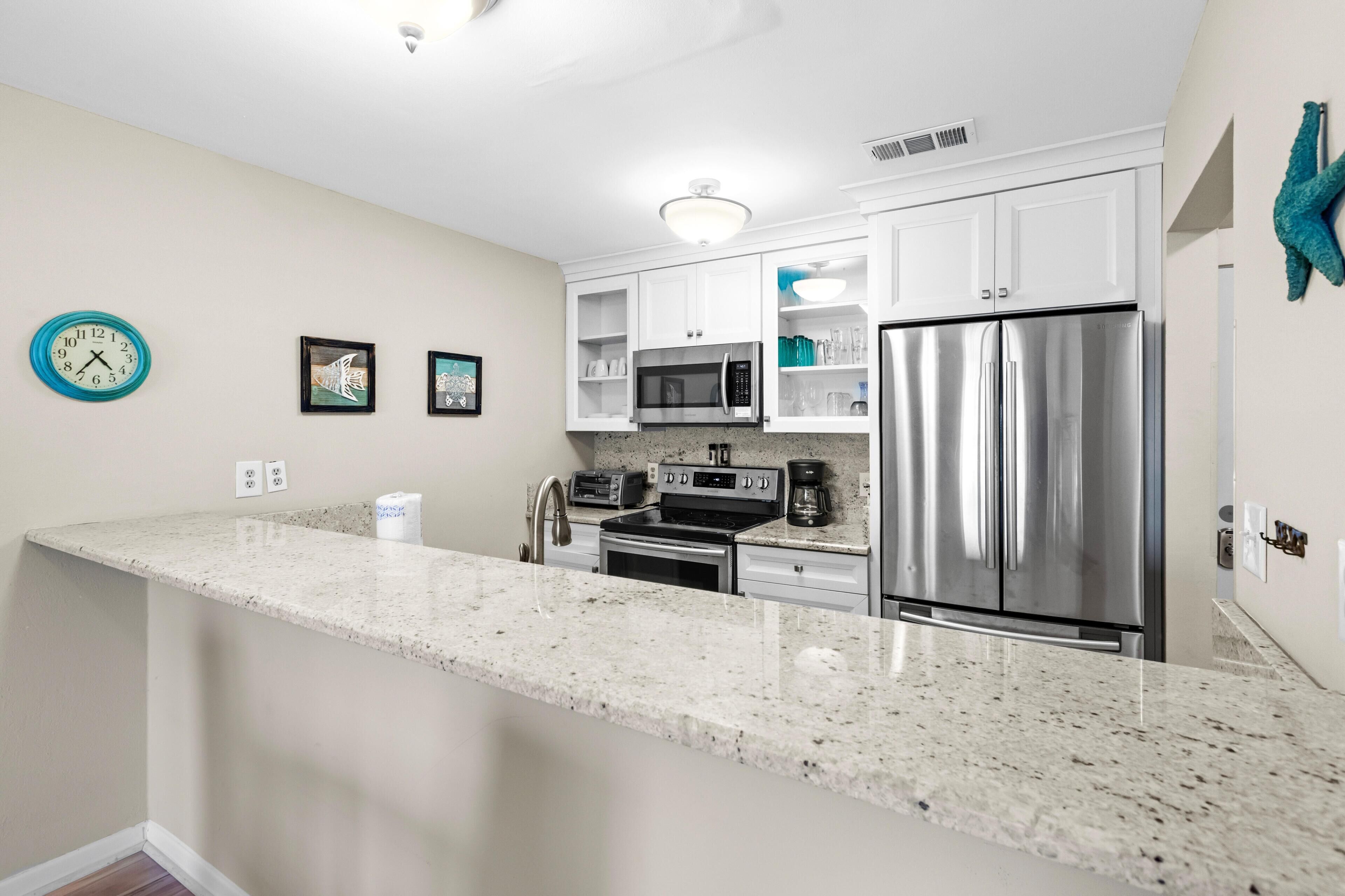 A kitchen with white cabinets, stainless steel appliances, a granite countertop, and a clock on the wall.