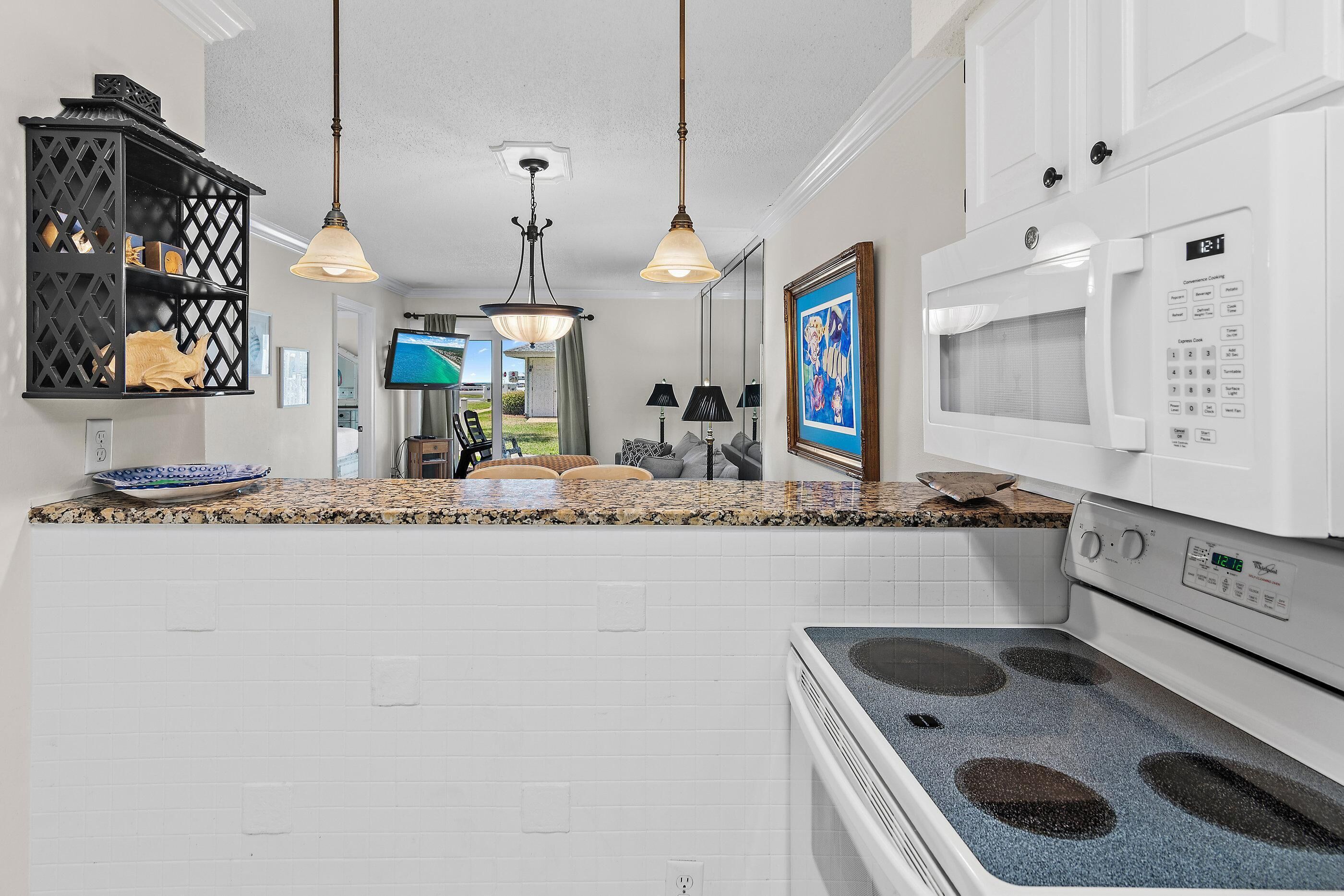 A kitchen with white cabinets, a microwave, an oven, granite countertops, and pendant lights.