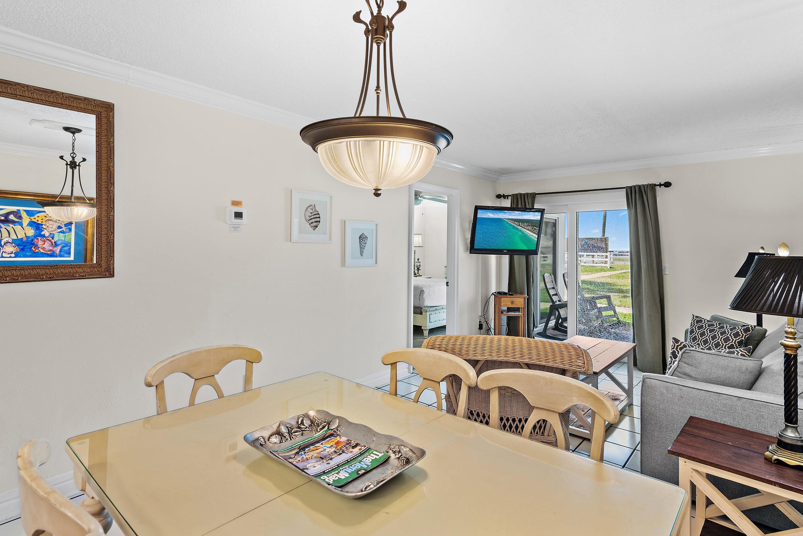 A dining area with a table, chairs, a chandelier, a television, and a view through the glass door.