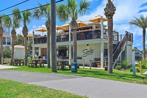 A two-story building with outdoor seating, palm trees, and a sign reading 'Sandoz Beachside.' - Tradewinds Condominium #2 (Miramar Beach)